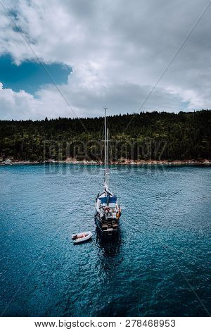 White Yacht Sailing In Calm Bay Near To Greek Shore. Dramatic Storm Cloudscape. Overcast Day, Dark S