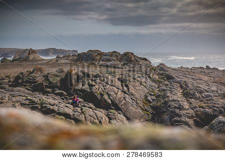 Young Woman Sitting On Rocks Near The Sea Of The Island Of Yeu