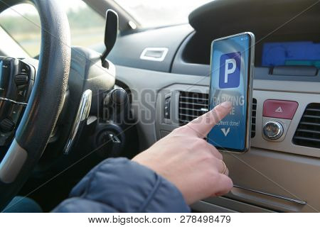 Driver using smartphone app to pay for parking in the paid parking zone in a city