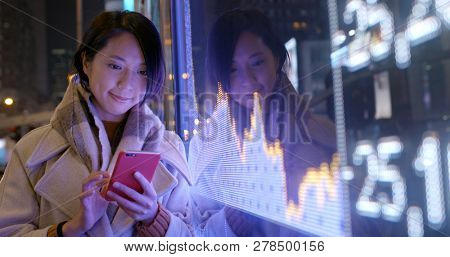Woman use of mobile phone to check the financial data in the street at night