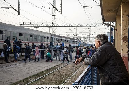 Sid, Serbia - November 14, 2015: Old Man Looking At A Group Of Refugees Boarding A Train To Cross Th