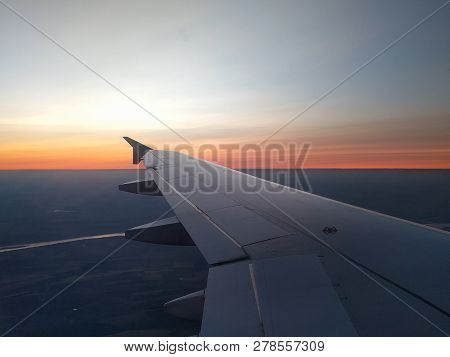 View From Airplane Window To Beautiful Sunrise Or Sunset. Wing Of Plane Flying Above In The Sky.