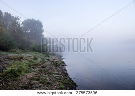 On The River Bank There Is An Abandoned Motor Ship On The Left Side. The Coast Is Covered With Grass