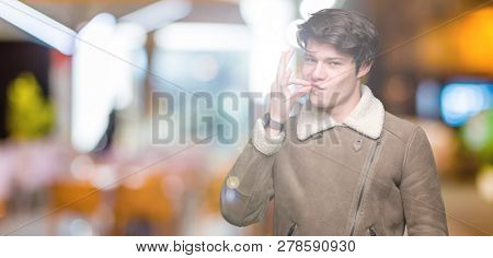 Young handsome man wearing winter coat over isolated background mouth and lips shut as zip with fingers. Secret and silent, taboo talking