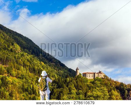 Middle-aged woman with backpack takes pictures of a beautiful landscape in the Dolomites. Wonderful day in South Tyrol. The concept of ecological and photo tourism