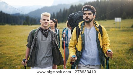 Gorup Of Friends Climbing Up Hill, With Backpacks And Climbing Stick