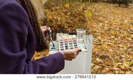 Close-up Of Young Girl Artist That Paints A Picture On The Easel In The Autumn Park