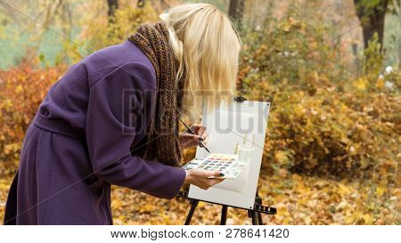 Close-up Of Young Girl Artist That Paints A Picture On The Easel In The Autumn Park