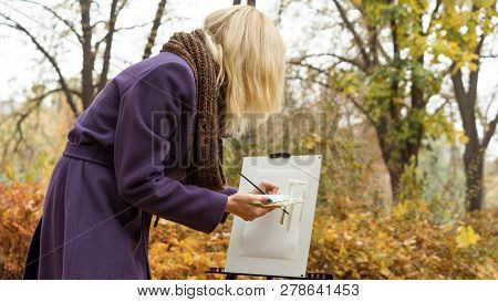 Close-up Of Young Girl Artist That Paints A Picture On The Easel In The Autumn Park