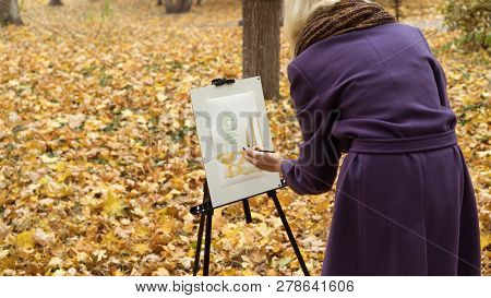 Close-up Of Young Girl Artist That Paints A Picture On The Easel In The Autumn Park