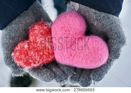 Hands In Wollen Gloves Holding Two Woolen Hearts Covered With Snowflakes