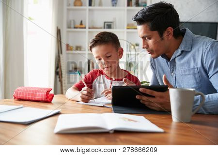 Hispanic pre-teen boy sitting at dining table working with his home school tutor