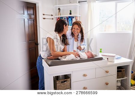 Millennial mother and grandmother playing with her baby son on changing table, selective focus