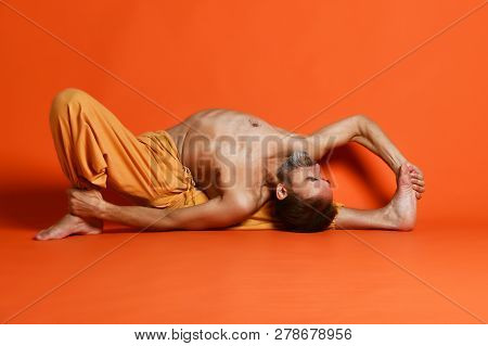Old Man Practicing Yoga Doing Stretching Exercises Against Orange Background