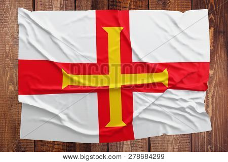 Flag Of Guernsey On A Wooden Table Background. Wrinkled Flag Top View.
