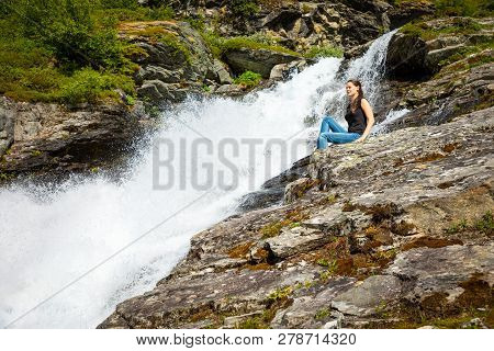 Young Woman Next To Waterfall In The Geiranger Valley Near Dalsnibba Mountain In Norway