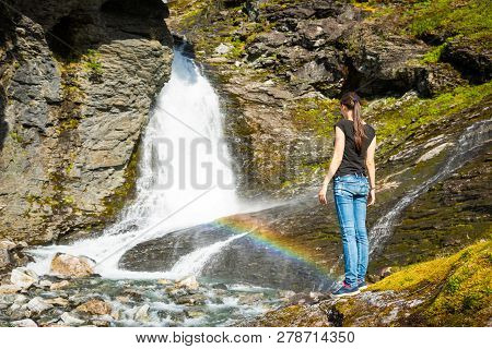 Young Woman Next To Waterfall In The Geiranger Valley Near Dalsnibba Mountain In Norway