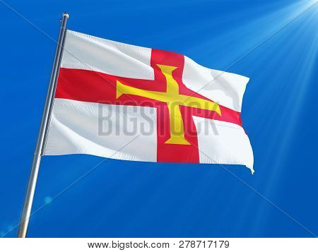 Guernsey National Flag Waving On Pole Against Deep Blue Sky Background. High Definition