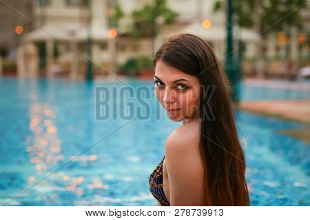 Portrait Of Sexy Woman Sitting On The Edge Of Swimming Pool, Wearing Bikini While On Vacations In A 