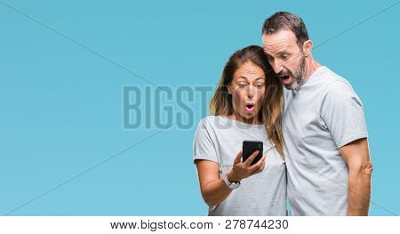 Middle age hispanic couple texting message on smartphone ver isolated background scared in shock with a surprise face, afraid and excited with fear expression