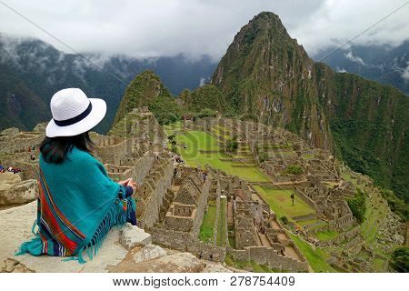 Female Traveler Sitting On The Cliff Looking At The Inca Ruins Of Machu Picchu, Unesco World Heritag