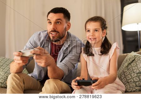 family, gaming and entertainment concept - happy father and little daughter with gamepads playing video game at home