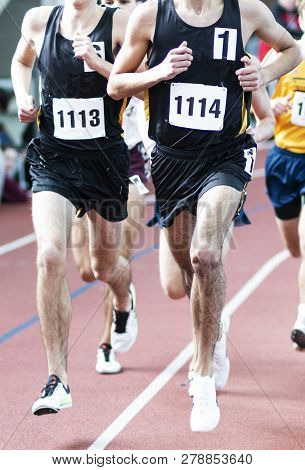 Two High School Boys From The Same Team Are Leading The Mile On An Indoor Track During A Race.
