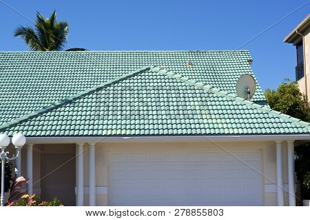 View Of Gray Tile Roof On Typical Generic Florida Home Showing Palm Tree And Blue Sky.