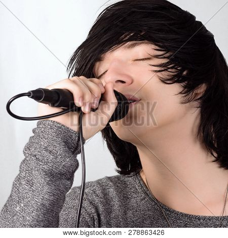 Black Hair Young Guy In Emo Style Is Singing In Microphone On White Background.