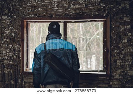 Man (adventurer)on Expedition Exploring Old Cottage In The Forest. Man In Blue Jacket Standing  In T