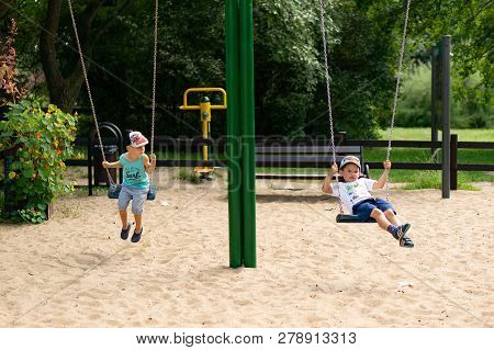 Poznan, Poland - July 29, 2018: Two Boy Sitting On A Swing At A Playground In The Cytadela Park. It 