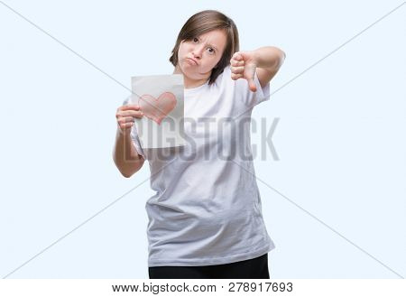 Young adult woman with down syndrome holding red heart card over isolated background with angry face, negative sign showing dislike with thumbs down, rejection concept