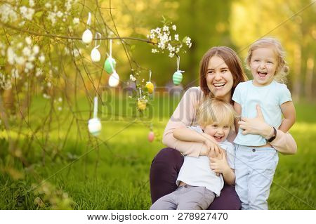Charming Little Children With Their Mother Hunting For Painted Eggs In Spring Park On Easter Day. Tr