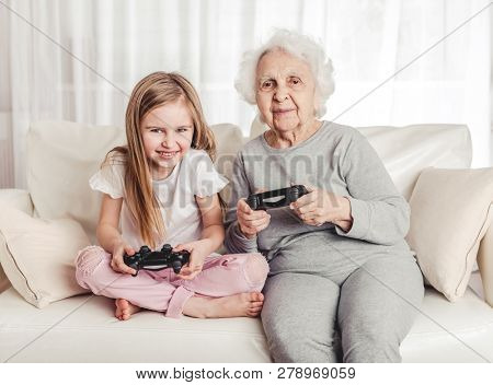 Smiling grandmother with little granddaughter playing games together with gamepads