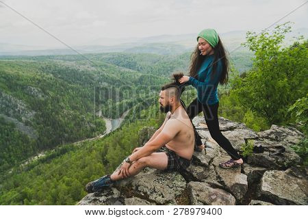 Asian Girl Doing Hair Style To Big Man On The Edge Of Rock In The Wild