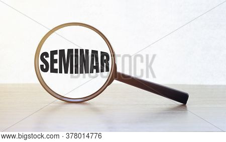 Magnifying Glass With Text Seminar On Wooden Table.