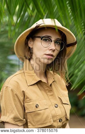 Woman Botanist Dressed In Safari Style In Greenhouse. Naturalist In Khaki Clothes, Leaver Gloves In 