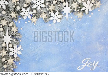 Festive Christmas border composition with silver joy sign, snow covered fir, white strs, snowflakes & ball bauble decorations on pastel blue background. Xmas & winter joyful concept.  Top view,  