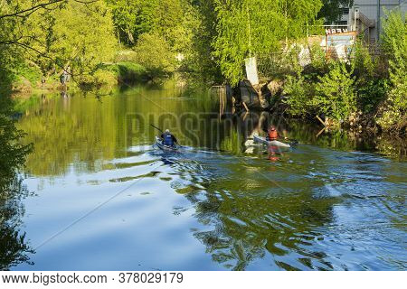 Two People Are Kayaking Along The City River On A Warm Sunny Day