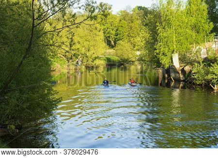 Two People Are Kayaking Along The City River On A Warm Sunny Day