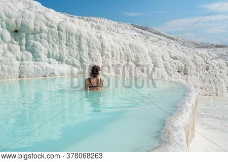 Woman in sunglasses bathing in travertine terraces pools in Pamukkale, Denizli, Turkey. Tourist relaxing in amazing white travertines