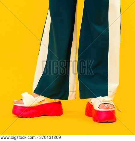 Women's Legs In Sport Sandals With Red Soles And Green Pants With Stripes On A Yellow Background.
