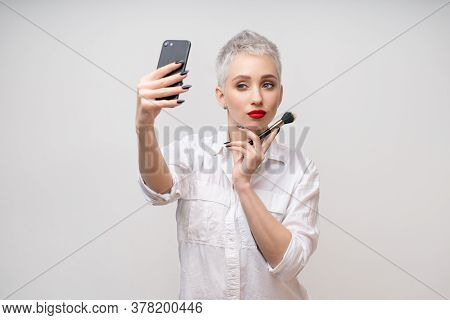 Studio Portrait Of Beautiful Trendy Girl With Short Hair Taking Selfie Via Cell Phone Over White Iso