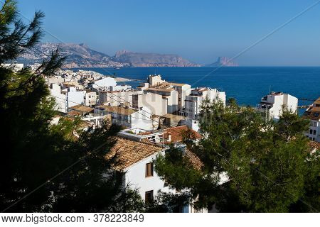 View Over The Sunlit White Washed Houses Between Fir Trees With Acient Roofs To The Ocean And The Ro