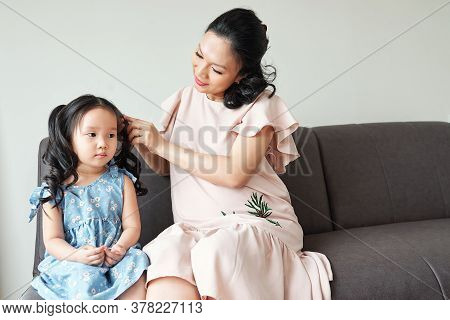 Pregnant Vietnamese Young Woman Braiding Hair Of Her Serious Little Daughter When Thay Are Getting R