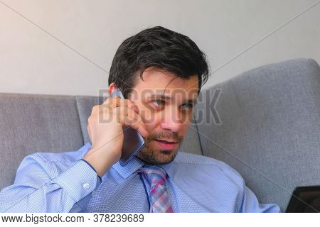 Portrait Of Man Working On Laptop Talking Smartphone Sitting On Couch At Home. Distant Work Of Offic