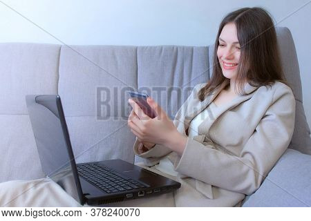 Woman Working Typing On Laptop And Reading Message On Smartphone Sitting On Couch, Distant Work. Cor