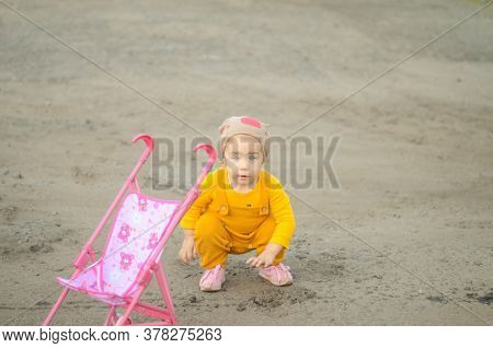 Photo Of A Toddler Girl In The Funny Hat Playing With A Toy Stroller