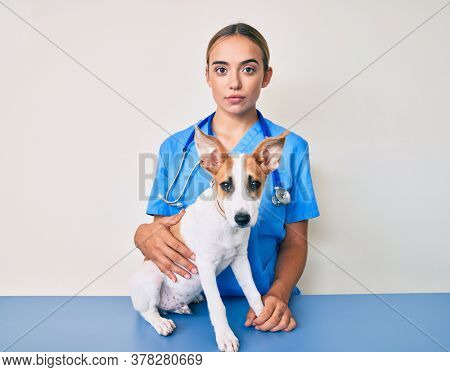 Young beautiful blonde veterinarian woman checking dog health thinking attitude and sober expression looking self confident 