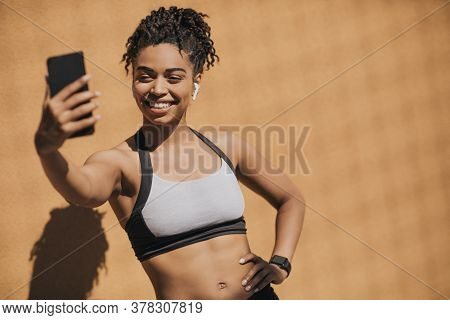 Sports Blog. Smiling African American Young Woman In Sports Bra With Wireless Headphones And Fitness